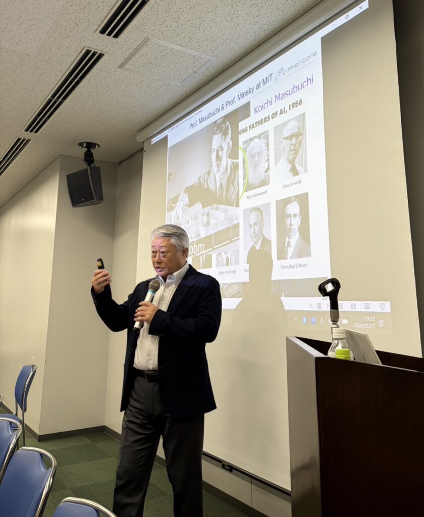 明治大学金融紫紺会 定例セミナーにて講演するサイファ・コア代表取締役CEO 中村宇利。スクリーンには、1956年の第1回ダートマス会議に集結したAIの父たちと、クロード・シャノン教授がロボットマウスを操作する場面、および増淵幸一（Koichi Masubuchi）教授に関するスライドが映し出されている。