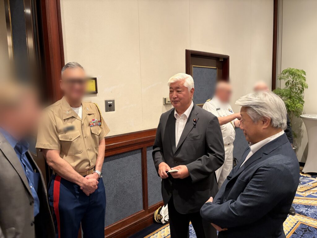 名刺を手にした前防衛大臣・中谷元氏と当社代表が、ISIC国家安全保障ランチョン会場で対話する様子。
